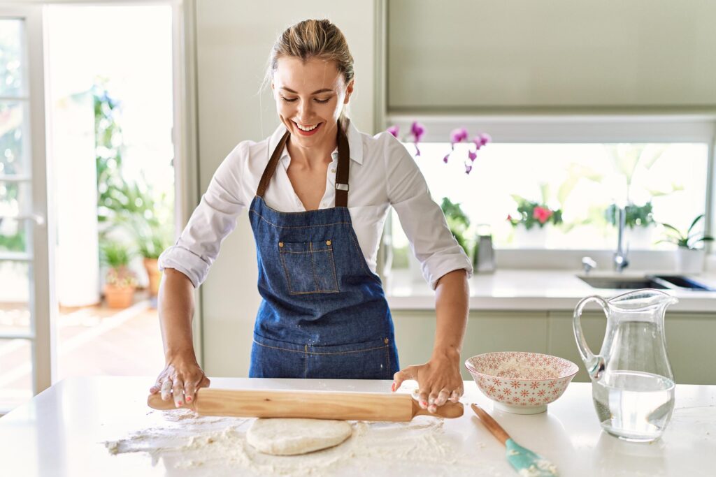 Blonde woman smiling kneading dough in kitchen while using these 6 baking tips